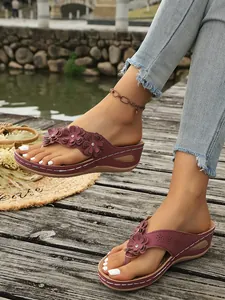 Detailopname van bordeauxrode sleehak slippers met bloemen op een houten steiger.