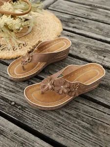Gedetailleerd zicht op bruine wedgesandalen voor dames met 3D-bloemdecoraties op de band.