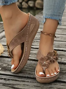 Close-up van stijlvolle bruine flip-flops met sleehak en 3D-bloemenaccenten voor dames