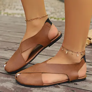 Detailansicht von stilvollen braunen flachen Sandalen mit Kreuzriemen auf Holzboden.