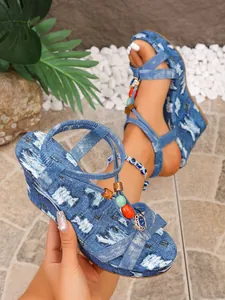 Detailansicht blauer Denim-Keilsandaletten mit bunten Perlenakzenten und modischen Kreuzriemen.