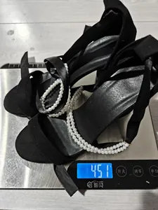 Detailed photo of black satin block heel sandals with pearls being weighed on a scale