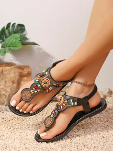 Stijlvolle boheemse platte teenslippers met gekleurde kralen op een kiezelachtergrond