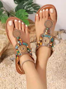 Detailweergave van boheemse teenslippers met kleurrijke kralen op het zand