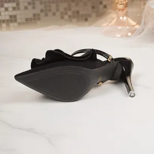 Detailed view of black pointed toe stiletto mules with ruffle trim on marble surface