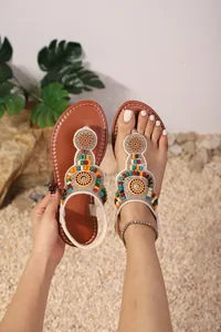 Gedetailleerd beeld van Boheemse teenslippers met gekleurde kralen op een zandgrond.