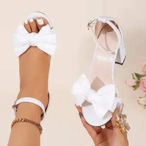 Close-up view of elegant white satin block heel sandals featuring an oversized bow detail
