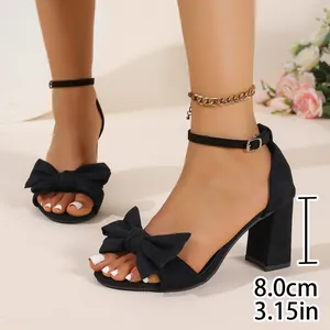 Detail showing black chunky heel sandals with elegant bow and adjustable ankle strap
