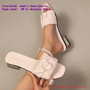 Detailopname van crèmekleurige slippers met geplooide band en stijlvolle strass blokhak