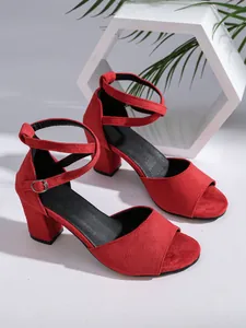 Elegant red suede sandals with chunky heels and ankle straps in a modern lifestyle setting.
