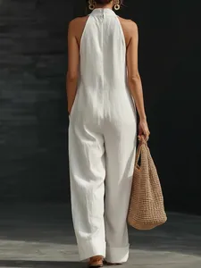 Back view of an elegant white sleeveless jumpsuit paired with a woven straw bag.