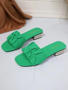 Detailweergave van groene sandalen met rimpels, lage strass-blokhakken en een vierkante neus