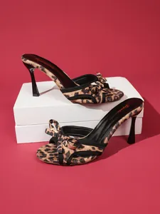 Leopard print mule sandals with bow detail and stiletto heels on a red backdrop