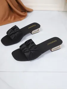 Detail van zwarte slippers met geplooide band en lage blokhak met glitter-inleg.