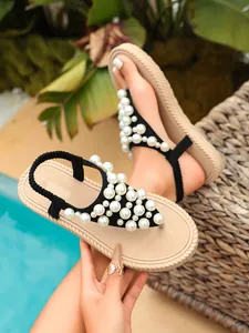 Dettaglio di infradito nere da spiaggia con eleganti decorazioni di perle bianche