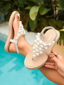 Vista dettagliata dei pesanti decori in perle su eleganti sandali infradito beige