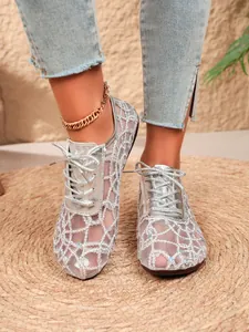Detailed view of silver mesh lace-up flats worn with denim and a gold anklet.