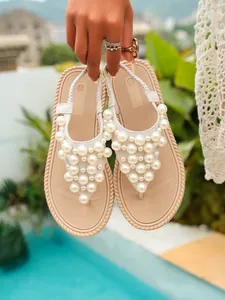 Dettaglio ravvicinato di eleganti sandali infradito beige decorati con perle bianche