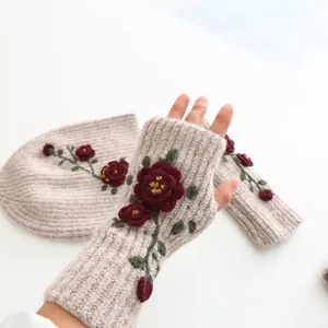 Close-up of beige knit fingerless gloves with red floral embroidery and matching beanie