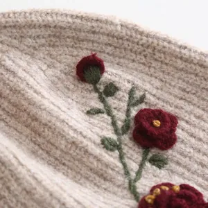 Macro view showing intricate red floral embroidery on beige knitted wool fabric texture