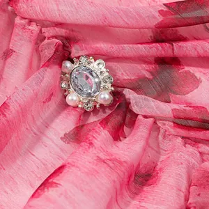 Détail macro d'une broche en cristal et perle sur un tissu de robe à fleurs roses