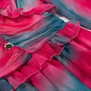Gros plan d'une robe dégradée rose et bleu sarcelle avec volants et broche.