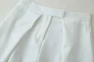 Detailed macro shot of the waistband and stitching on white high-waisted trousers.