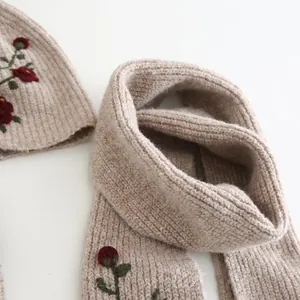 Detailed close-up of beige ribbed knit hat and scarf set with elegant red rose embroidery