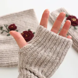 Detailed macro view of knit fingerless gloves featuring elegant red rose embroidery