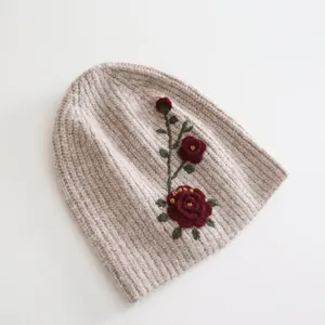 Detail shot of exquisite red flower embroidery on warm oatmeal knitted beanie hat