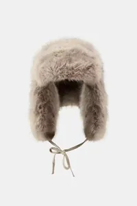 Detail view of a fluffy light grey faux fur trapper hat with a bow tie closure for winter.