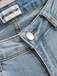 Gros plan sur un jean évasé bleu clair délavé montrant le bouton et les surpiqûres.