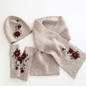 Detail of beige knit winter set featuring red floral embroidery on hat scarf and gloves