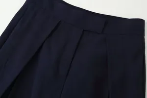 Detail of navy blue wide-leg trousers showing pleated waist and twill fabric texture