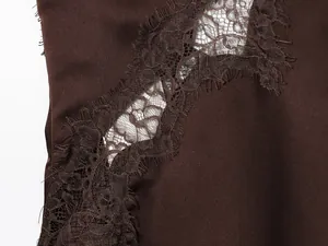 Gedetailleerd macrobeeld van fijn kantborduurwerk op een donkerbruine satijnen camisole.