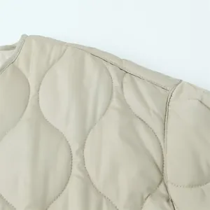 Detail van de gegolfde wattering op de schouder van een lichtbeige gewatteerde jas