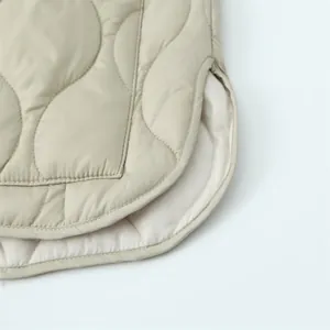 Detailopname van de gewatteerde zoom van een beige lichtgewicht winterjas van katoen