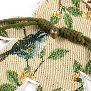 Detailopname van een geweven konijn patch met bloemen- en vogelmotieven en groen koord