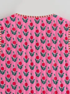 Macro detail of pink quilted vest featuring red floral pattern and striped trim