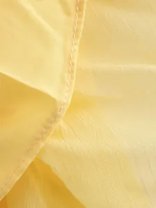 Gros plan du tissu d'une jupe plissée jaune montrant la texture froissée et les coutures