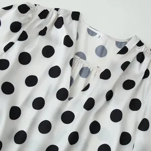 Close-up of a white V-neck blouse with classic black polka dots and size S tag