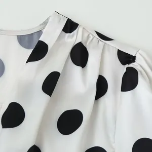 Macro shot of black polka dots and pleated shoulder details on elegant white blouse