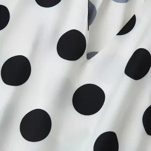Detailed close-up showing the high-quality white and black polka dot fabric and V-neck design.