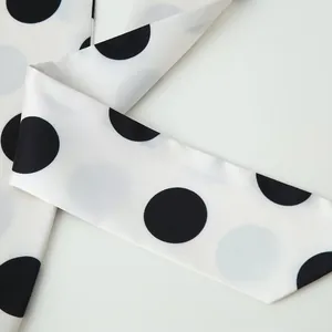 Close-up detail of white and black polka dot satin fabric from a stylish women's clothing set