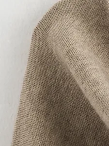 Nahaufnahme der weichen, hellbraunen Strickstofftextur eines Damenmantels
