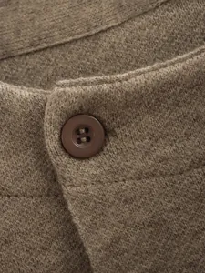 Makro-Detail eines braunen Strickmantels mit feinem Gewebe und Knopfverschluss.