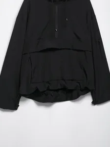 Dettaglio di una giacca a vento nera con cappuccio e tasca a marsupio funzionale.