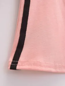 Close-up van de roze stoftextuur en zwarte zijstreep op een kledingstuk in retrostijl.