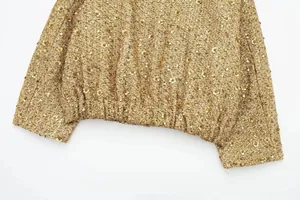 Makrodetail einer goldenen Pailletten-Tweedjacke mit schimmernder Textur und Saum