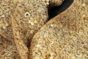 Nahaufnahme einer goldenen Paillettenjacke mit Tweed-Textur und floralen Verzierungen